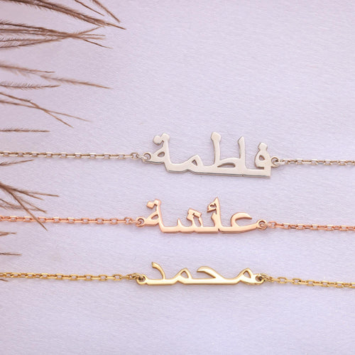 May include: Three gold necklaces with Arabic name pendants. The top necklace features the name 'Fatima', the middle one says 'Aisha', and the bottom one displays 'Mohammad'. Each necklace is a delicate chain with the name in a stylized Arabic script.