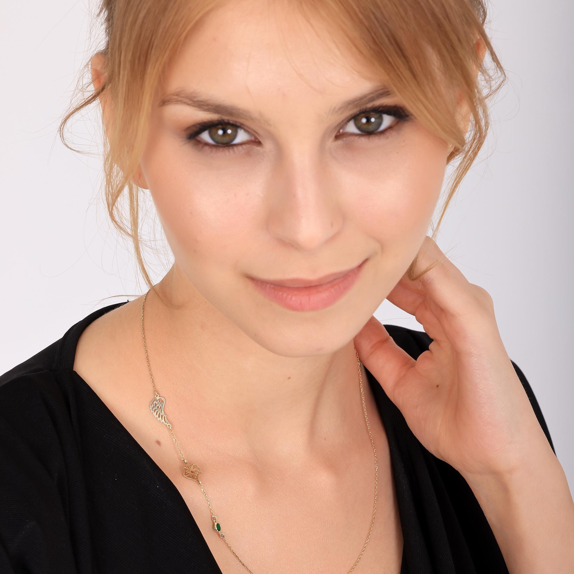 Close-up of a woman wearing a delicate gold-toned necklace featuring multiple charms, including a birth flower, angel wing and small birthstones, with her face partially visible.