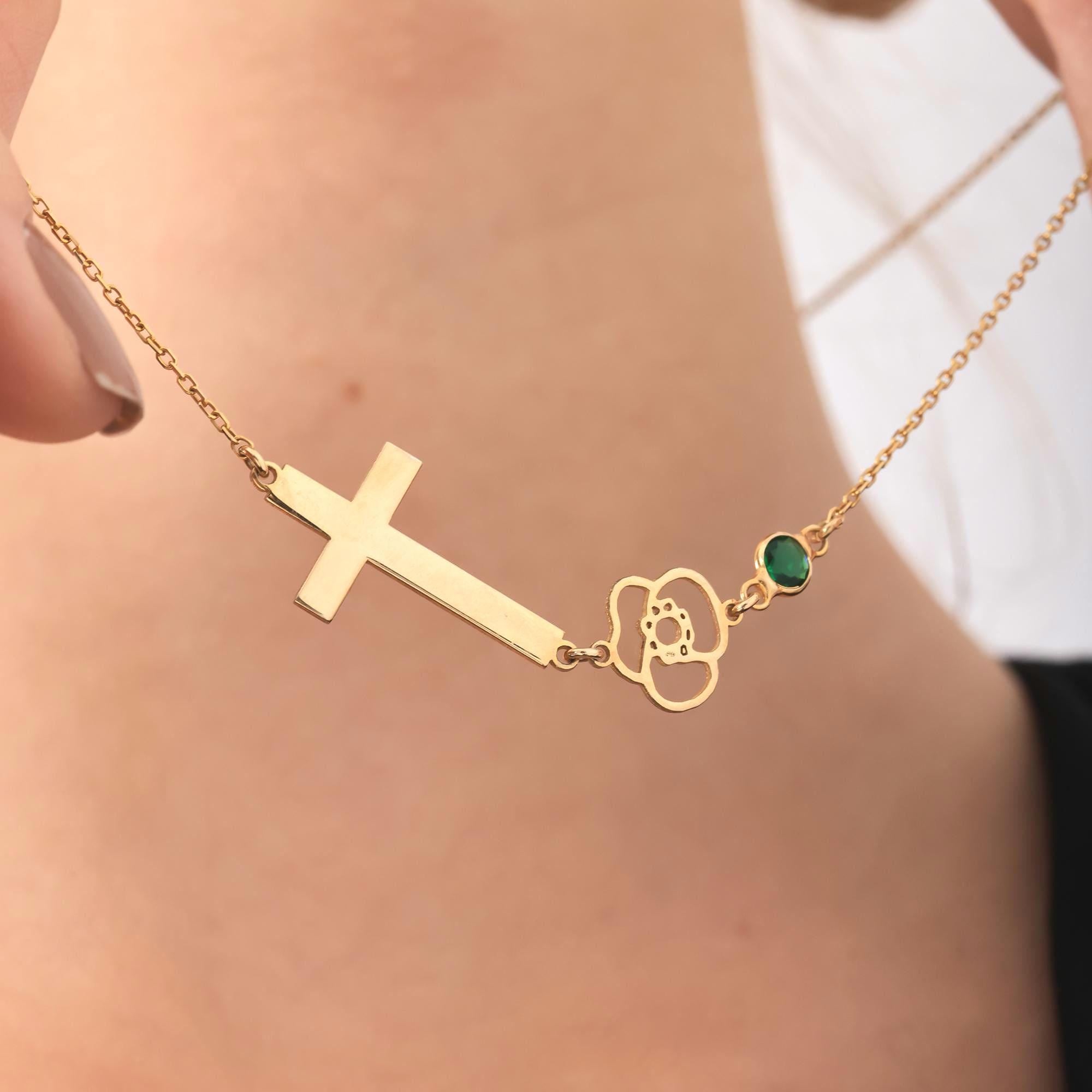 A gold chain necklace with a cross pendant, a flower pendant, and a green gemstone accent.