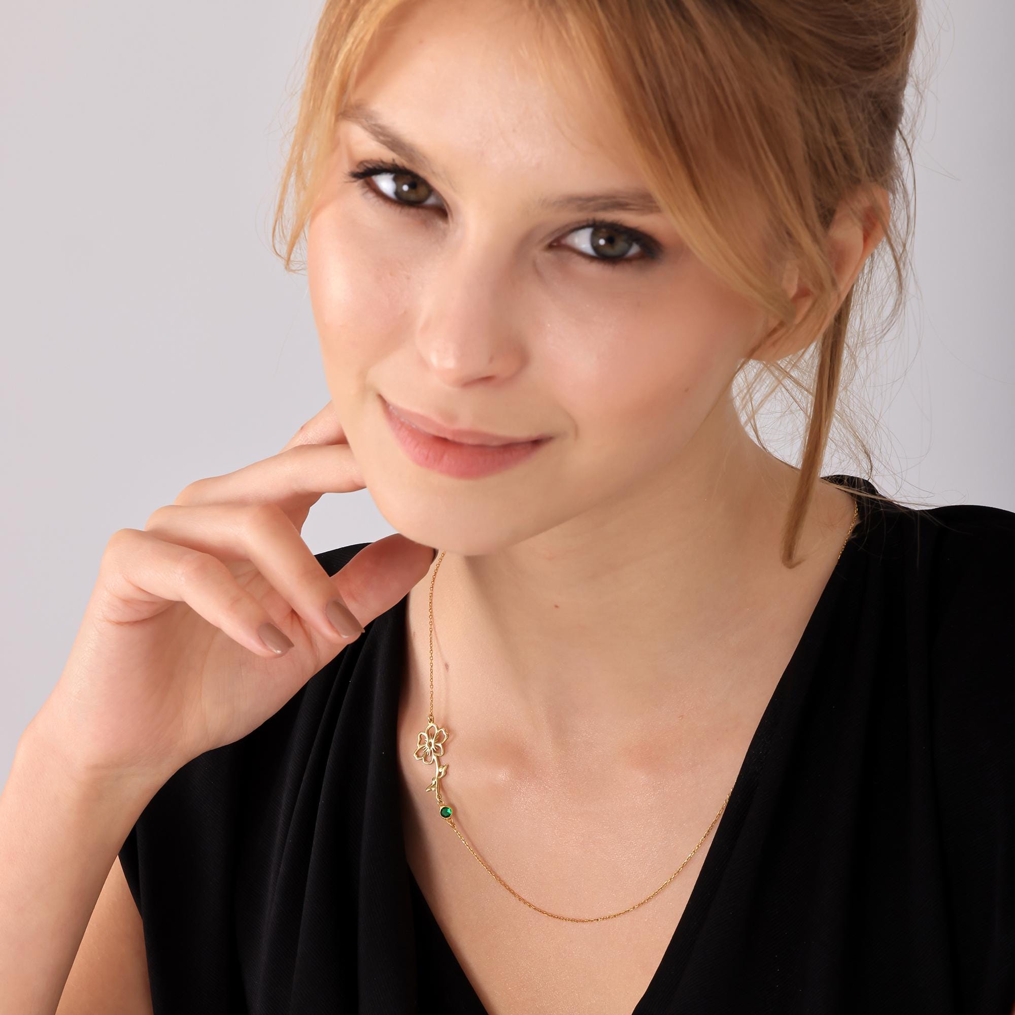 May include: A gold chain necklace with a green gemstone and a gold flower pendant.